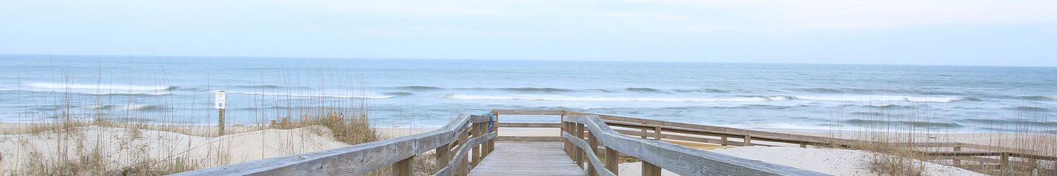 A wooden boardwalk leads down to the beach and ocean through the dunes