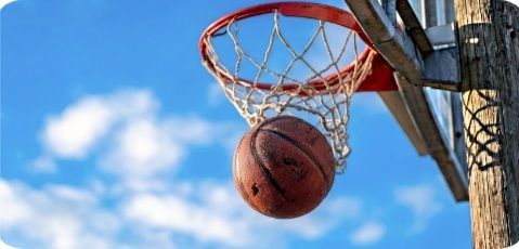 Basketball entering the hoop from below on an outdoor court with a blue sky. The ball is in the net against a clear day.