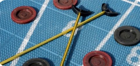 Two croquet mallets crossed over red and black croquet balls on a blue lawn with wickets nearby.